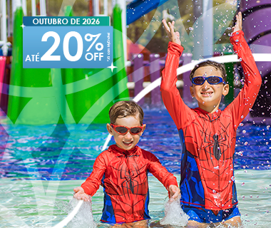 Duas crianças com roupas de super-herói brincam com jatos de água na piscina infantil perto de tobogãs.