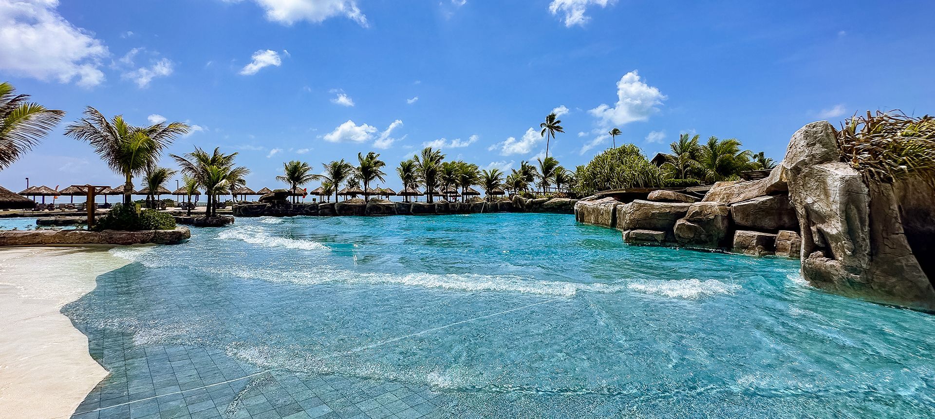 Wave pool with crystal-clear water, artificial rock formations, and coconut trees.