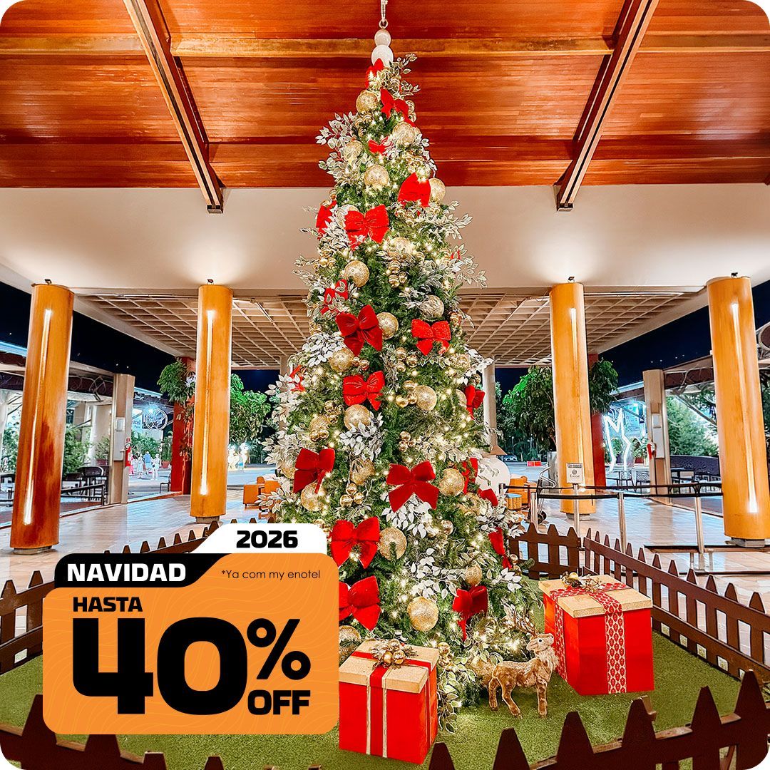 Grande árvore de Natal iluminada, decorada com laços vermelhos e bolas douradas, junto a caixas de presentes no resort Enotel. A imagem exibe o selo da promoção My Black com até 40% de desconto para reservas de Natal em 2026.