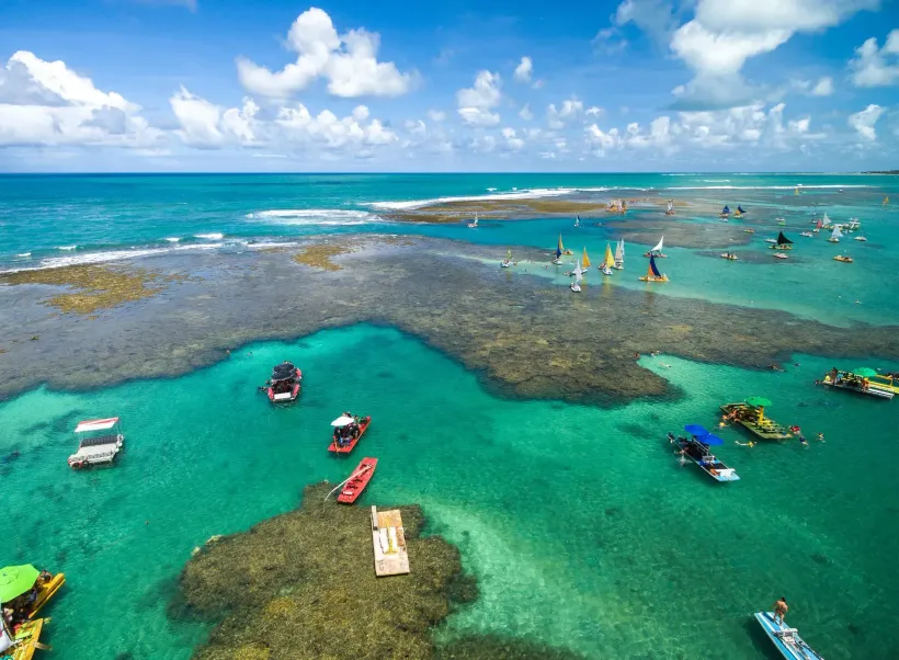Vista aérea de drone do mar turquesa com jangadas navegando entre os recifes de corais nas piscinas naturais de Porto de Galinhas
