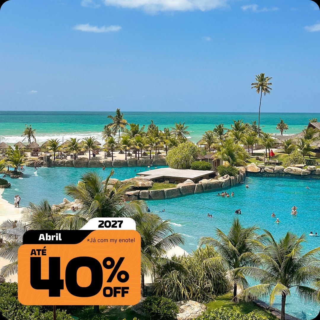 Vista aérea ampla das piscinas do resort Enotel, cercadas por coqueiros e áreas de lazer, com o mar verde-esmeralda de Porto de Galinhas ao fundo. A imagem contém o selo da promoção My Black com até 40% de desconto para reservas em abril de 2027