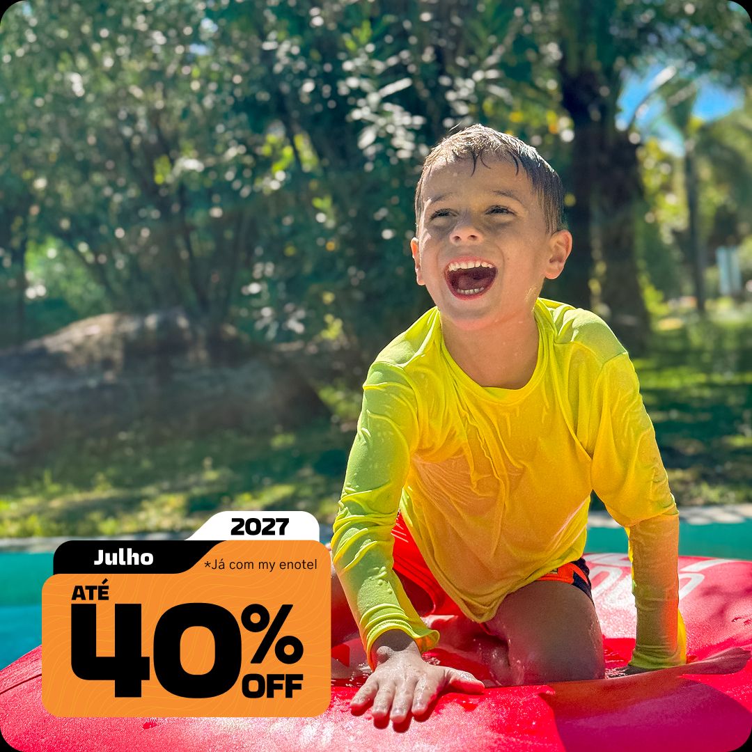 Menino sorrindo e se divertindo em uma boia vermelha na piscina do resort Enotel, com muita natureza ao fundo em um dia de sol. A imagem apresenta o selo da promoção My Black com até 40% de desconto para reservas em julho de 2027