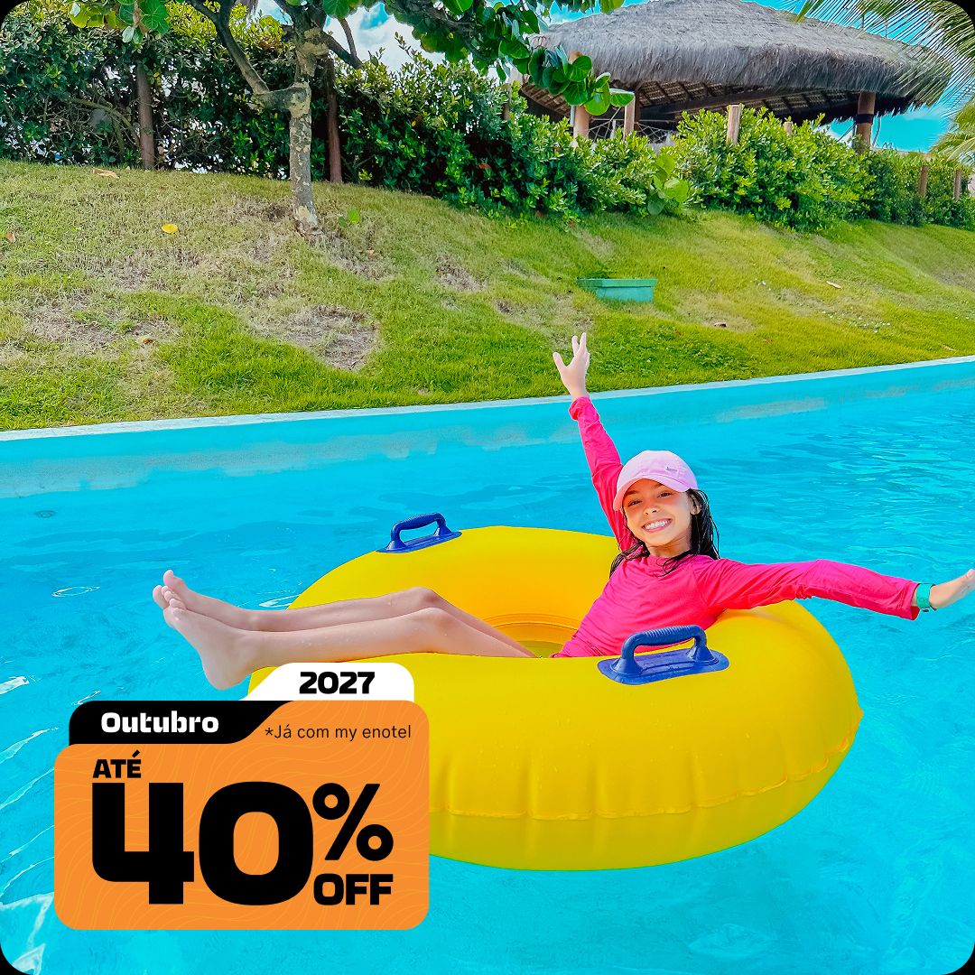 Menina sorrindo e acenando com os braços enquanto brinca em uma boia amarela no rio lento do resort Enotel, em um dia ensolarado. A imagem contém o selo da promoção My Black com até 40% de desconto para reservas em outubro de 2027.