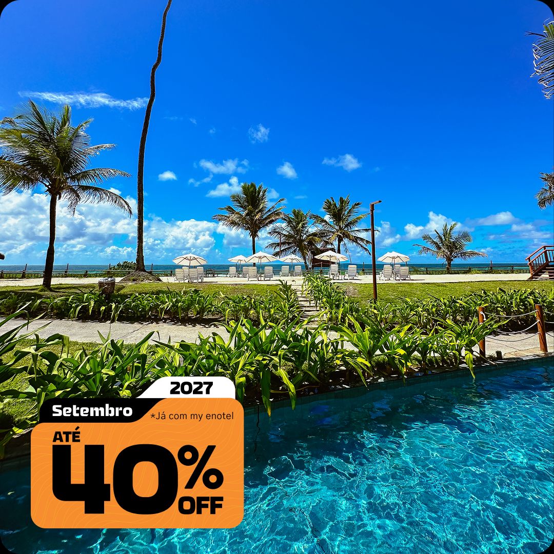 Vista a partir da piscina do resort Enotel, com vegetação verde levando a guarda-sóis na areia da praia e o mar azul ao fundo. A imagem contém o selo da promoção My Black com até 40% de desconto para reservas em setembro de 2027