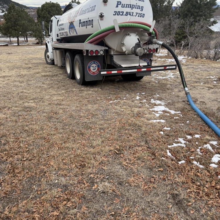 White pumping truck on dry grass, hose connected at rear, working in a rural area.