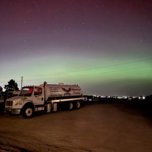 White tanker truck parked at dusk under a green aurora-lit sky over a dark open lot