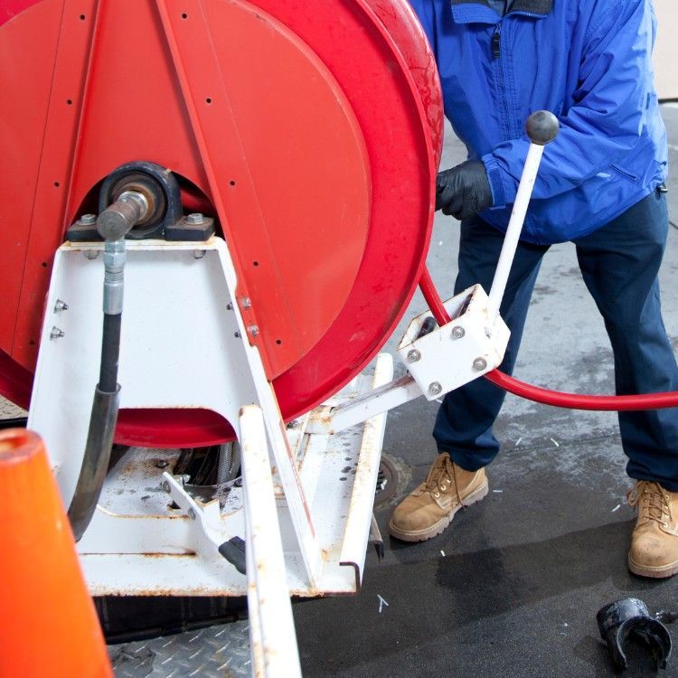Worker operating a large red hose reel on wet pavement