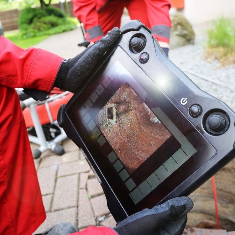 Gloved hands holding a handheld device showing a live view of a brick wall outdoors