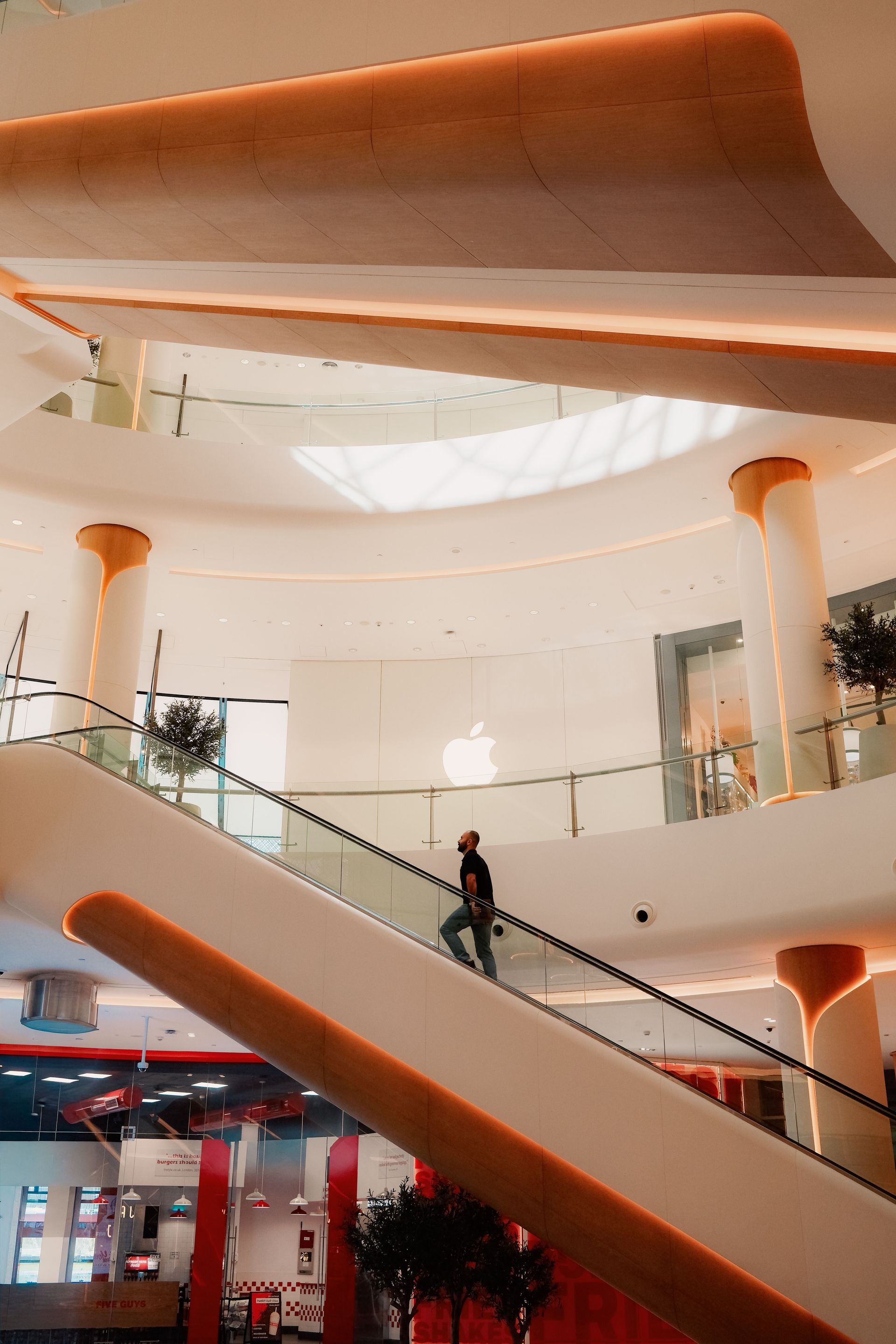 Interior de un centro comercial moderno con escaleras mecánicas curvas de color naranja y una persona caminando.