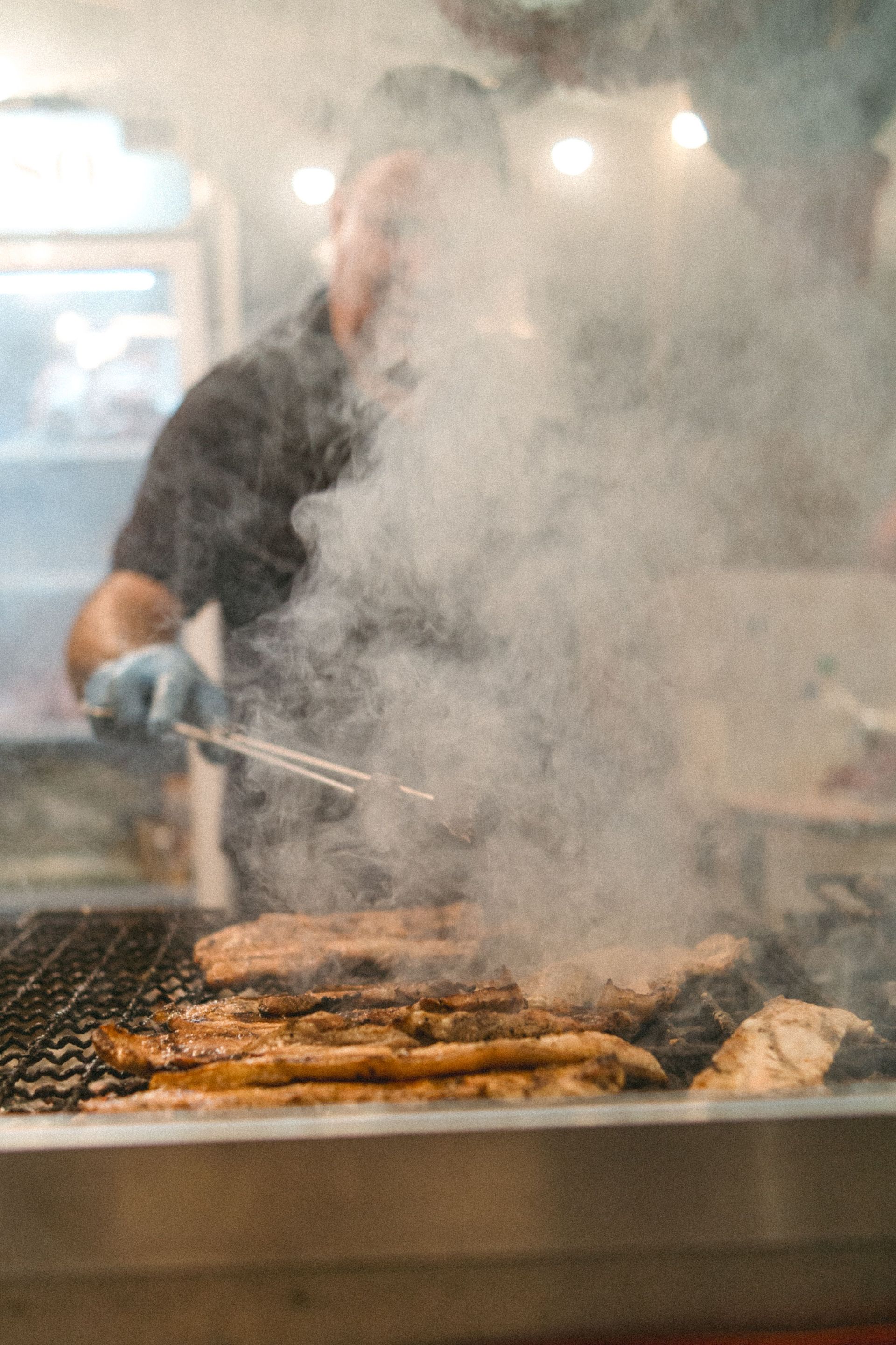 Cocinar carne a la parrilla en una barbacoa humeante en una cocina o puesto de comida.
