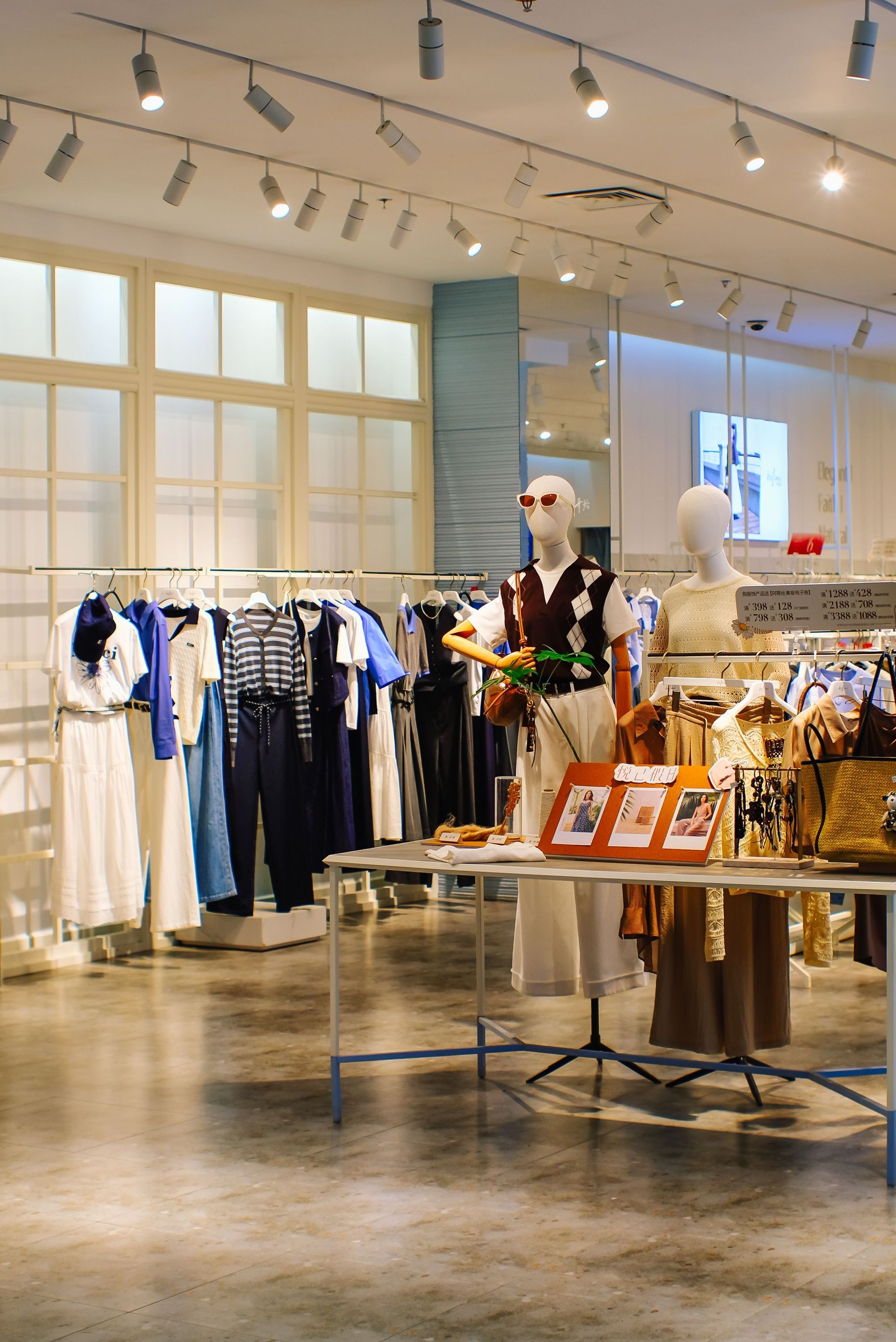 Interior de una tienda de ropa con percheros de vestidos, maniquíes y una mesa de exposición bajo iluminación direccional.