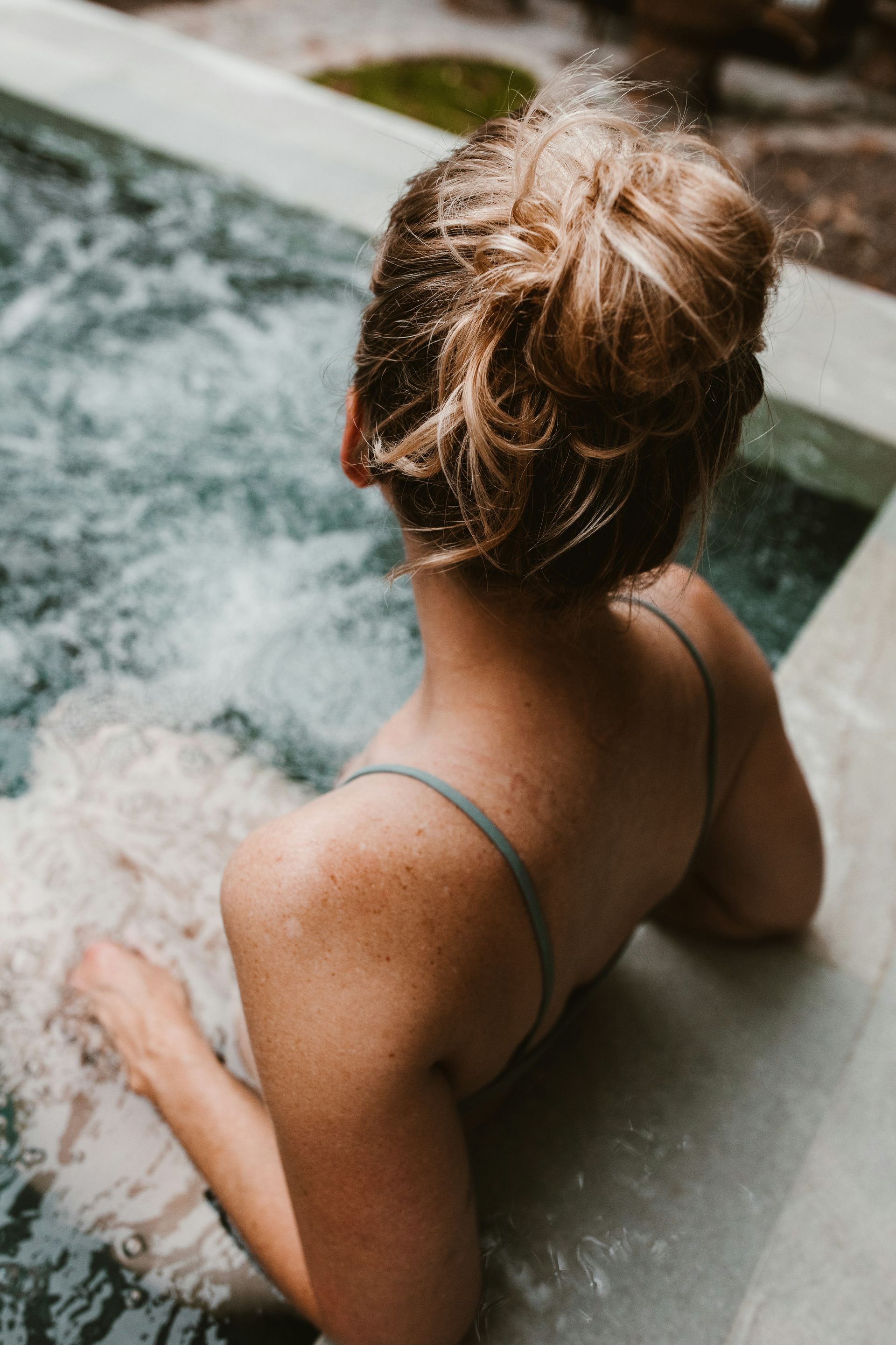 Persona en un jacuzzi, vista desde atrás, con el pelo recogido en un moño y agua salpicando a su alrededor.