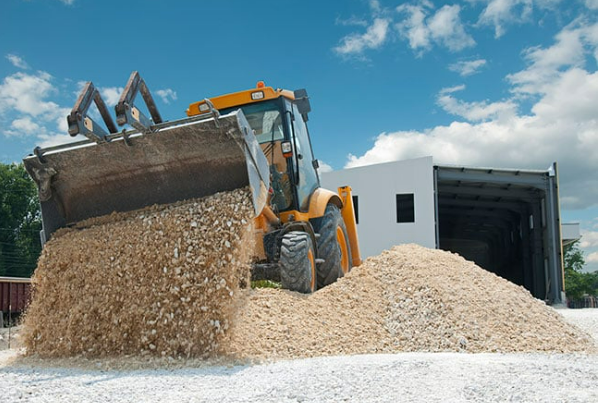 A bulldozer is loading a pile of gravel into a container