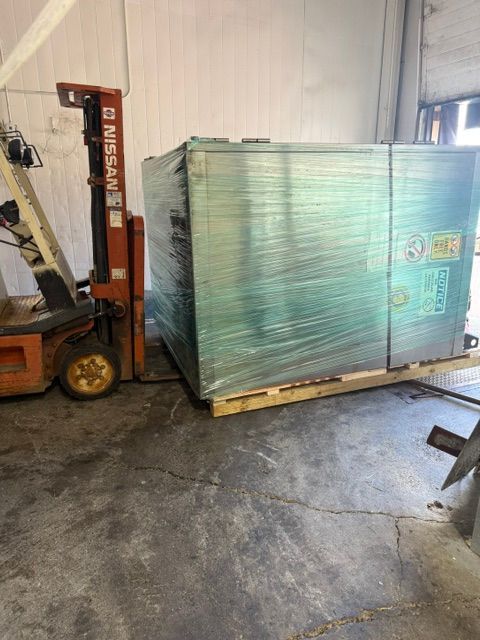Forklift moving a wrapped palletized crate in a warehouse.