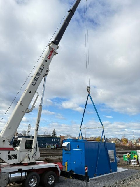 Crane lifting a blue shipping container on a cloudy industrial site