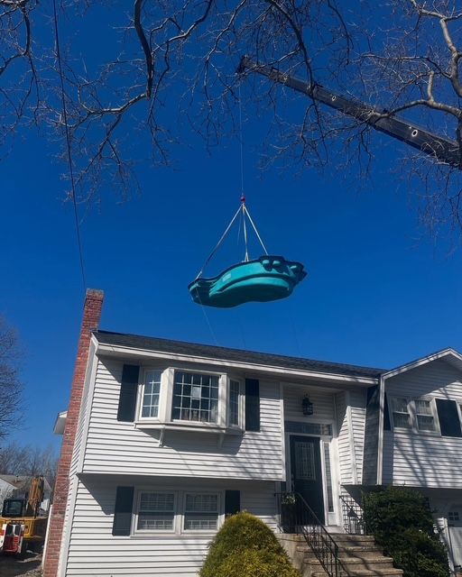 Teal kayak hoisted above a white house under a clear blue sky, framed by bare tree branches