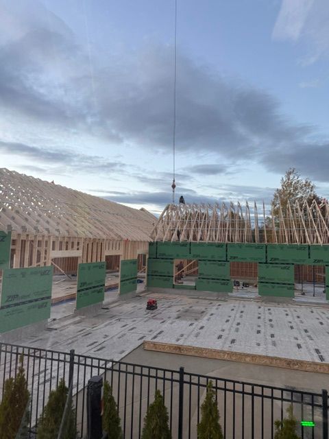 Courtyard with green construction barriers, black fence, and cloudy sky; unfinished roof in the background