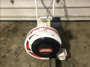 A little wonder blower is sitting in front of a garage door.