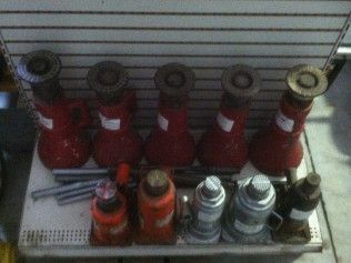 A bunch of red bottle jacks are sitting on a shelf.