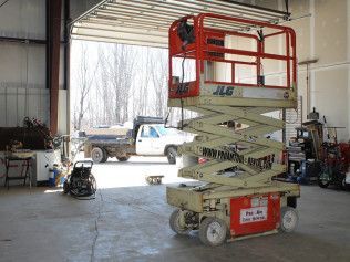 A scissor lift is parked in a garage next to a truck.