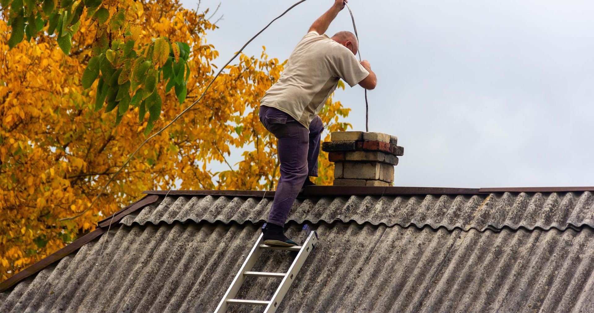 A man on a ladder atop a roof, performing chimney repair in Cary, IL, showcasing skilled craftsmansh