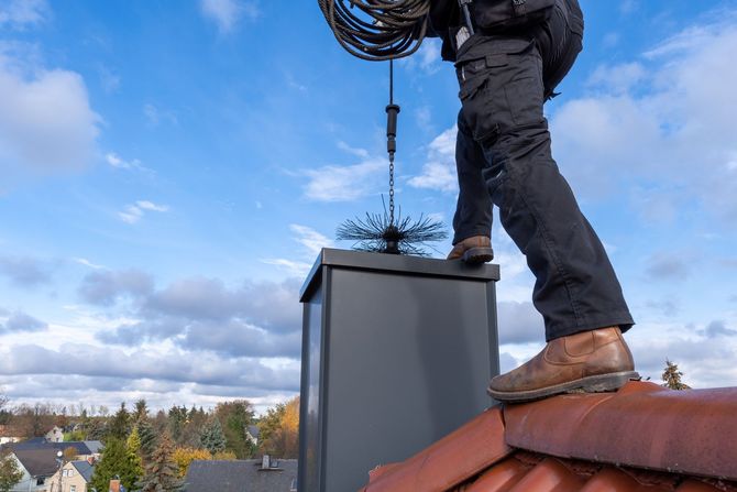 Chimney sweep on a roof cleaning a chimney with brush; blue sky background.