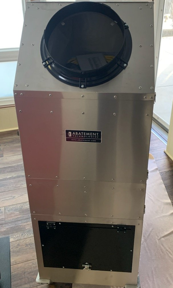 Silver industrial machine with a large black circular top, a rectangular black opening at the bottom, and a label.