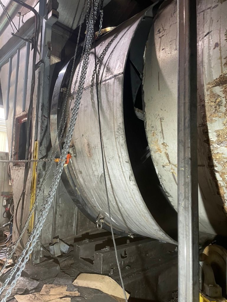A large metal pipe is being lifted by chains in a factory.