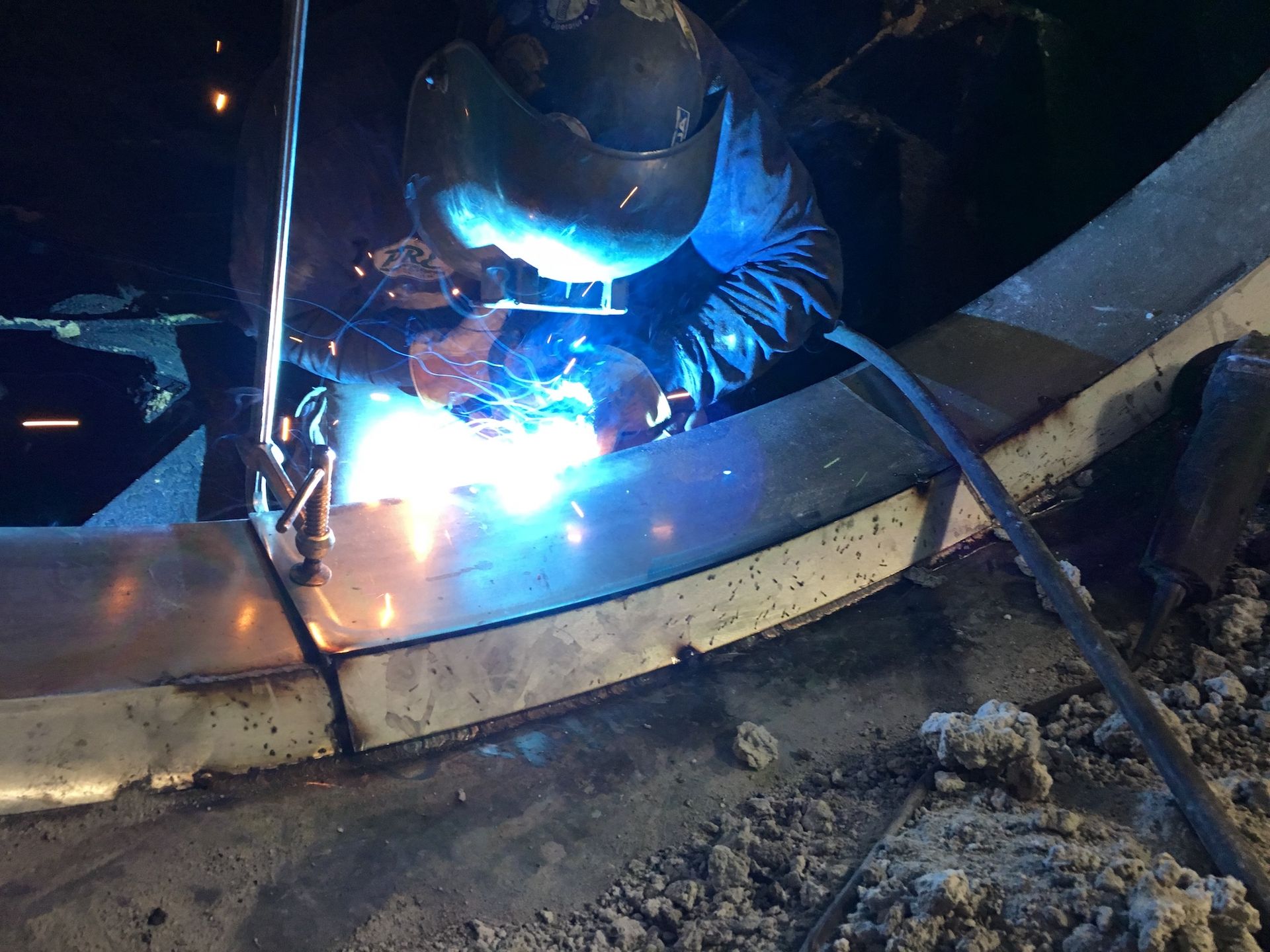 A man is welding a piece of metal in a dark room.