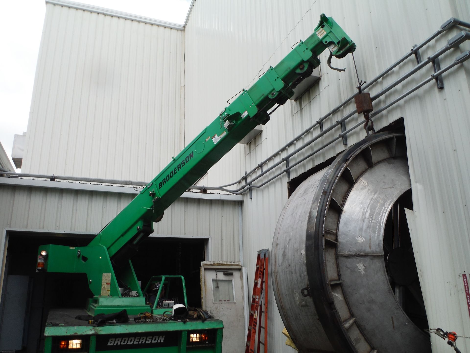 A green crane is lifting a large metal object