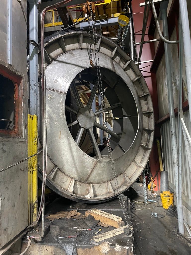 A large fan is being lifted by a crane in a factory.