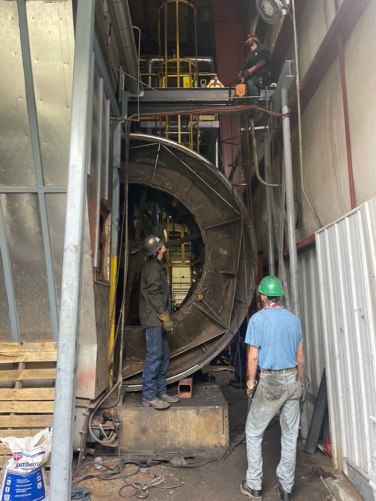 A man wearing a green hard hat is standing in front of a large metal object.