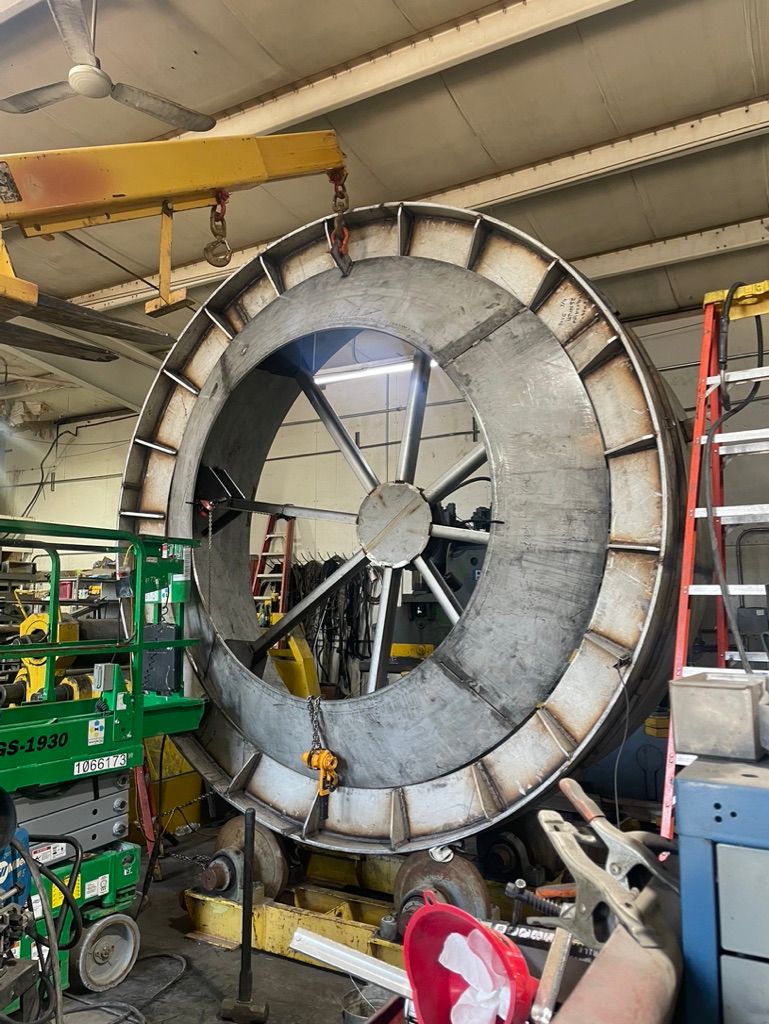 A large metal wheel is being built in a factory.