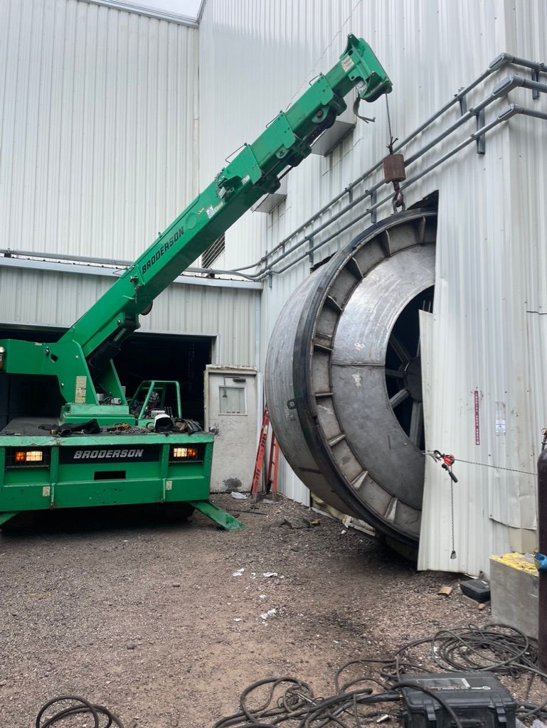 A green crane is lifting a large metal object in front of a building.