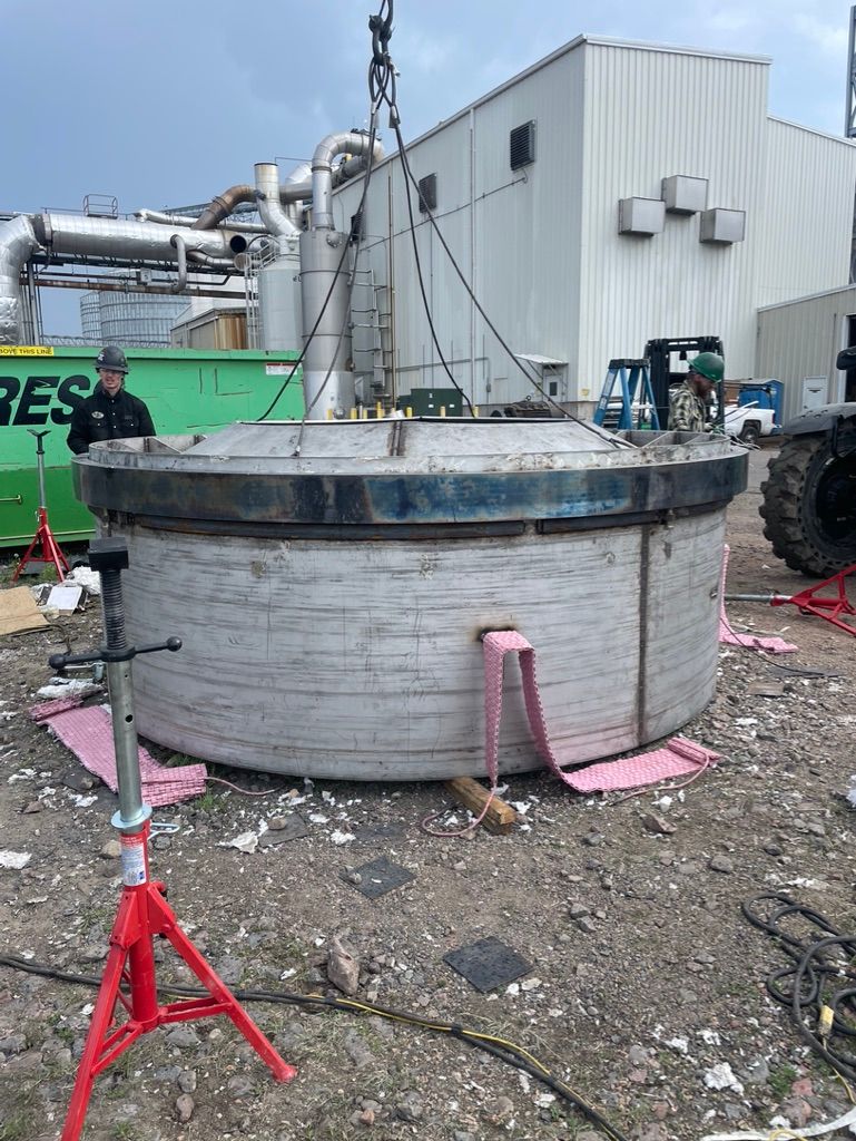 A large metal object is being lifted by a crane in front of a building.