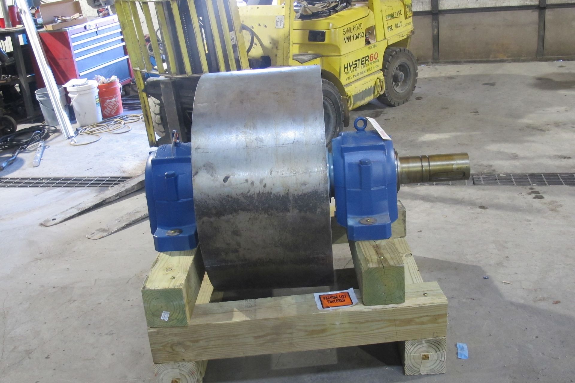 A machine is sitting on a wooden pallet with a forklift in the background