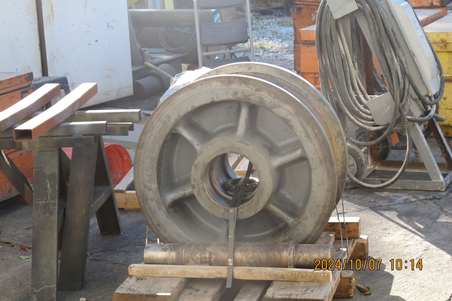 A large metal wheel is sitting on a wooden pallet.