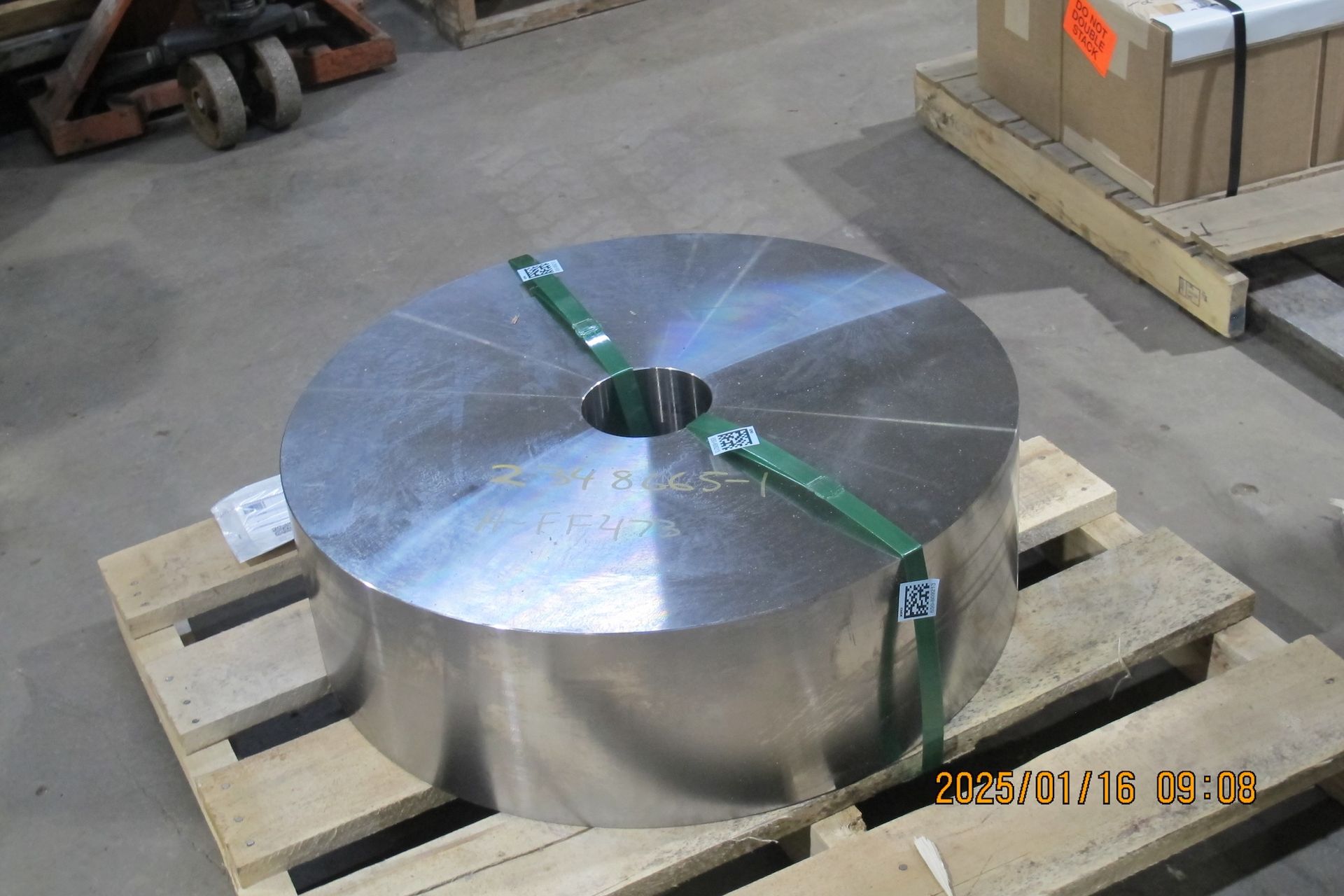 A large metal disc with a hole in the middle is sitting on a wooden pallet