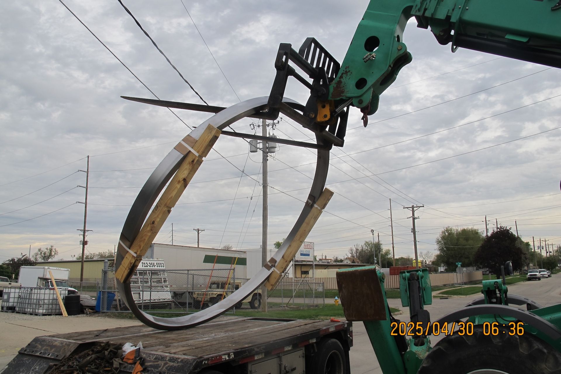 A green crane is lifting a large piece of metal