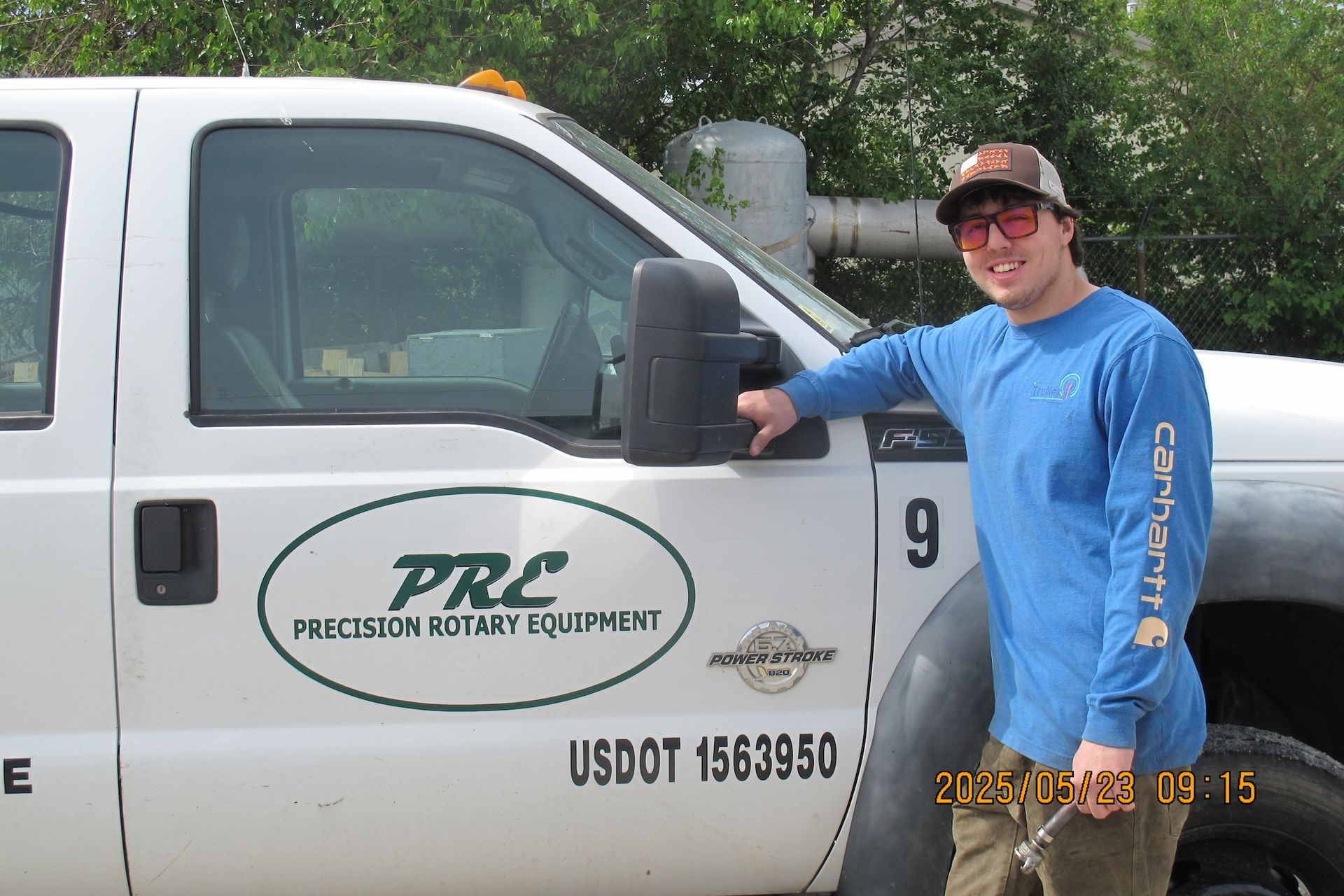A man in a blue shirt is standing in front of a truck that says prc
