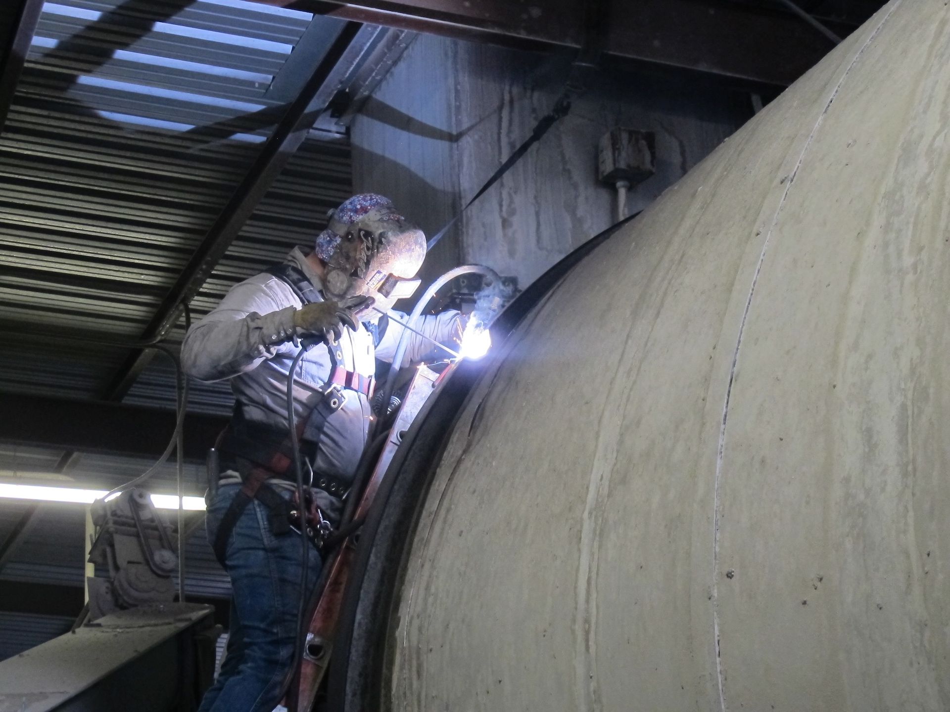 Two men are welding a large pipe in a factory