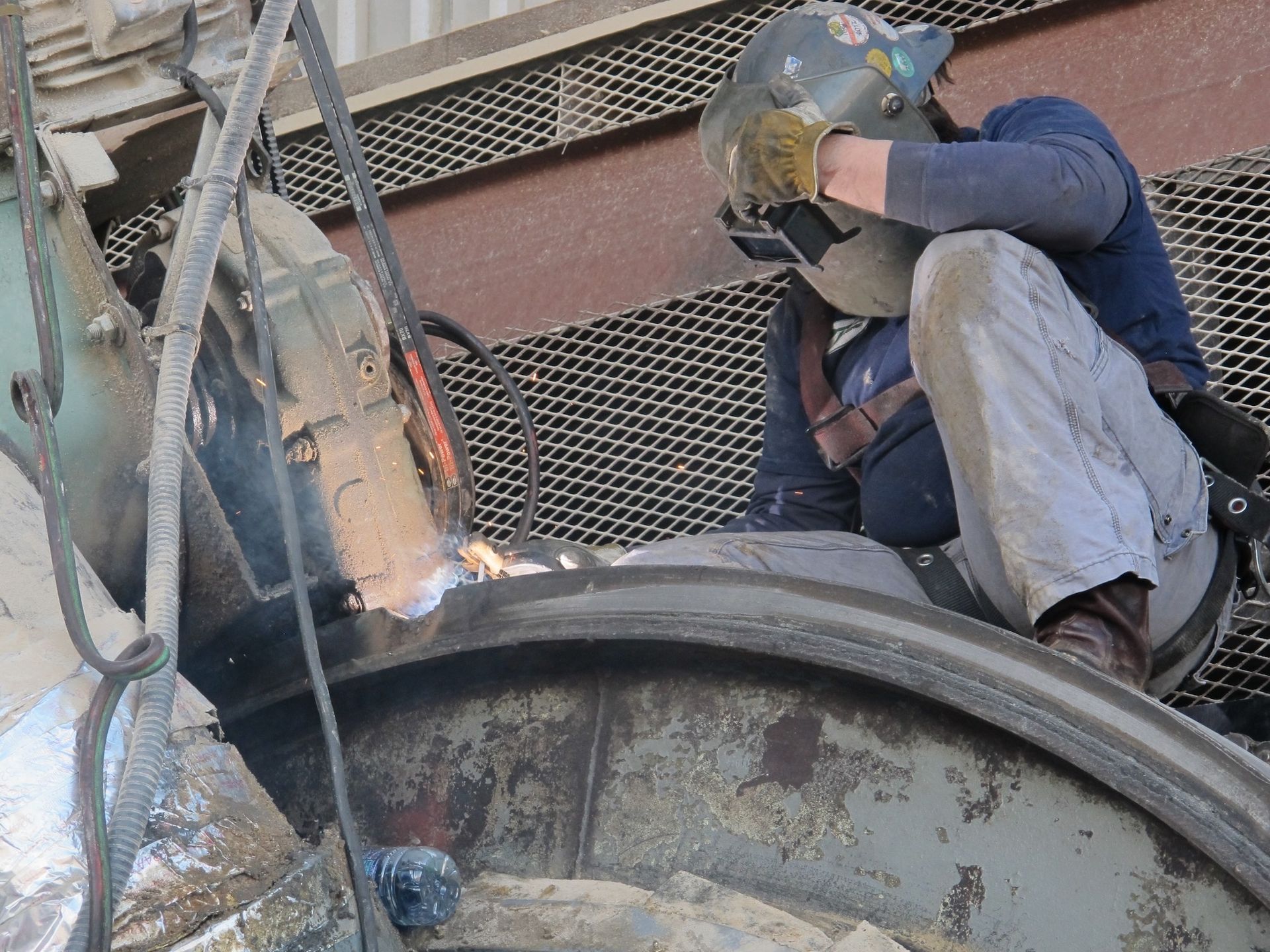 A man wearing a welding helmet is welding a piece of metal