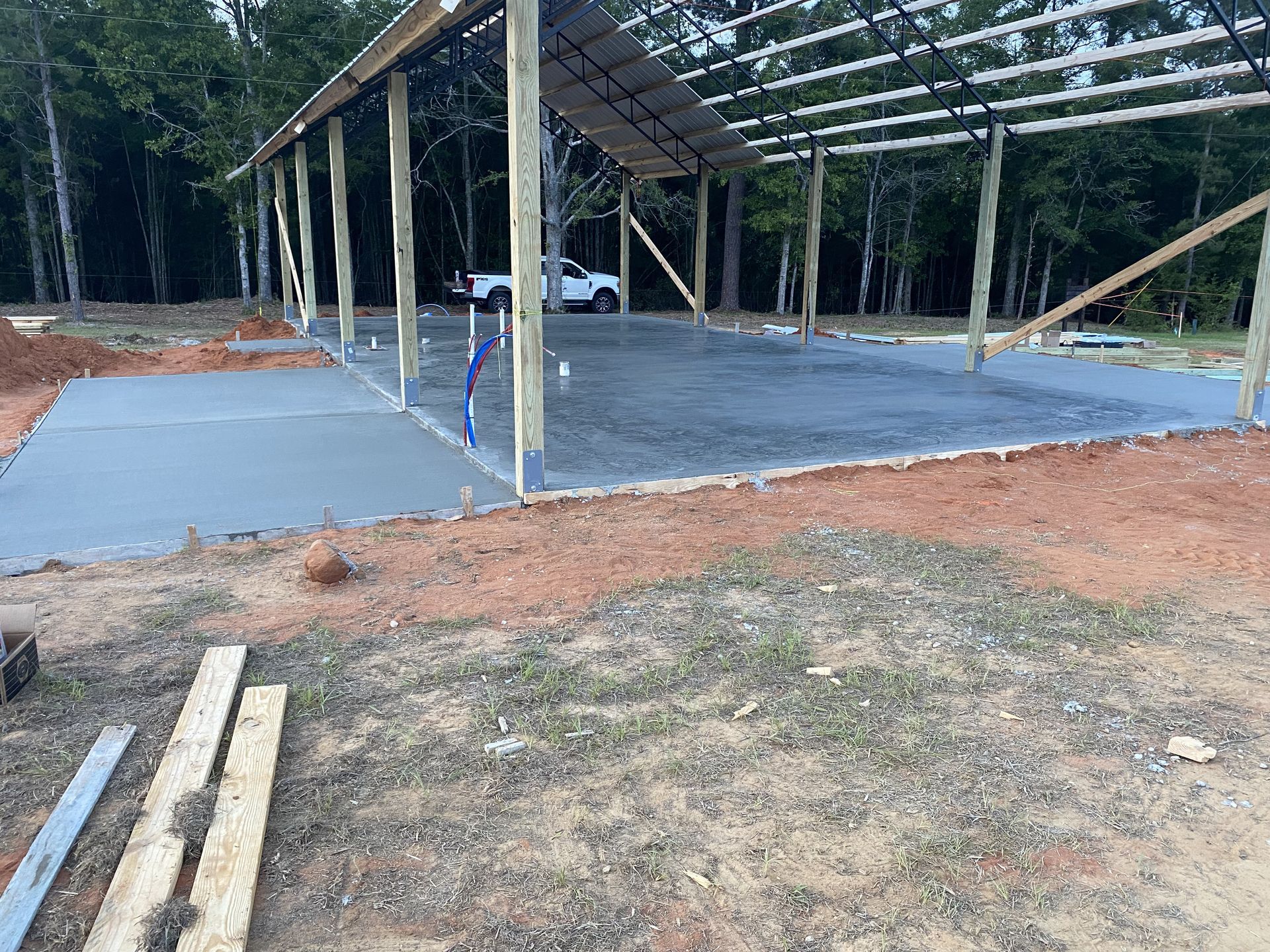 Newly poured concrete floor under a partially built metal roof structure with wood posts.