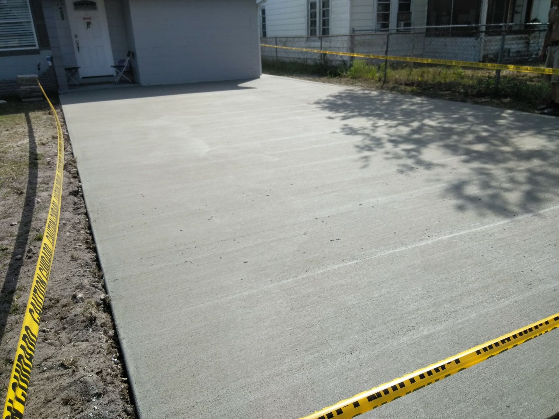 Newly poured concrete driveway with caution tape in front of a house.