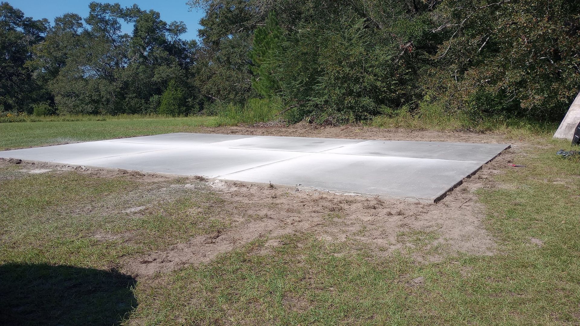 Concrete slab on a grassy area, surrounded by dirt and vegetation in a yard.