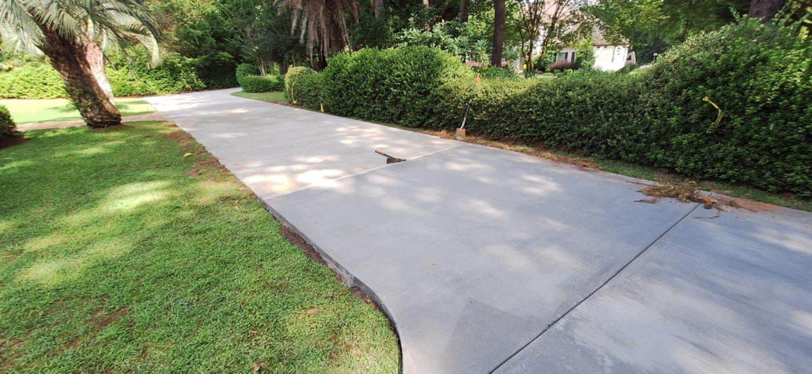 A concrete pathway curves through a green, grassy area lined with hedges and trees.