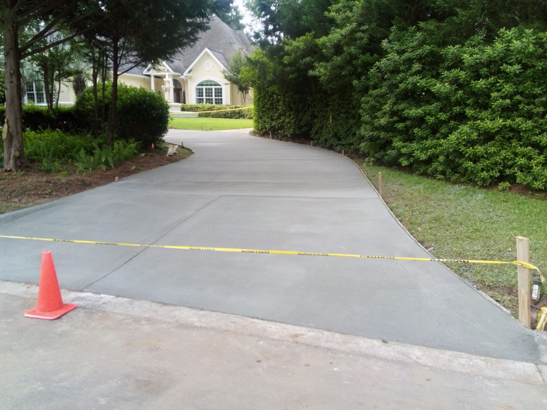 Newly poured concrete driveway with caution tape and traffic cone leading to a house.