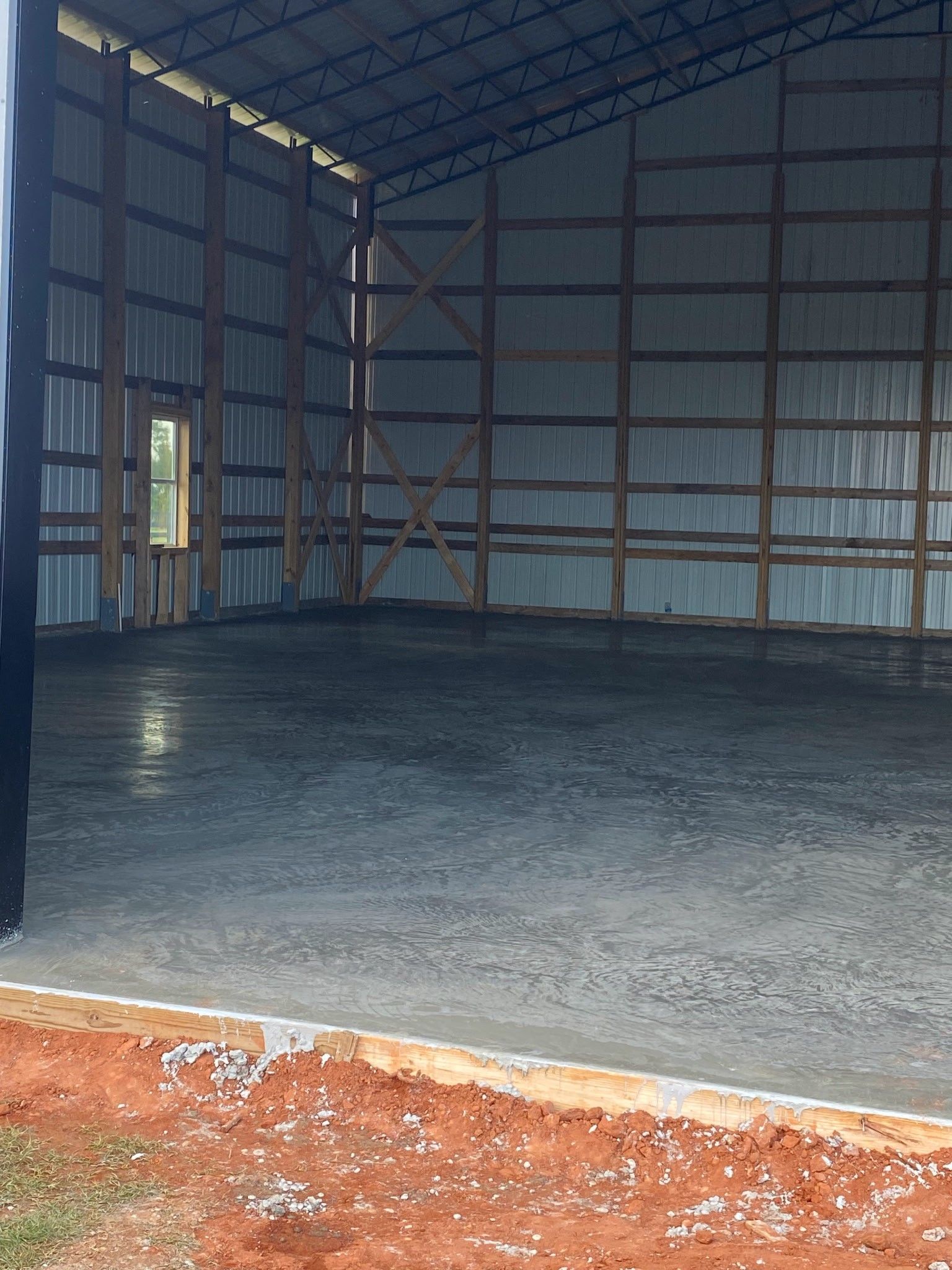 Interior of a large metal building with a concrete floor and wooden support beams.