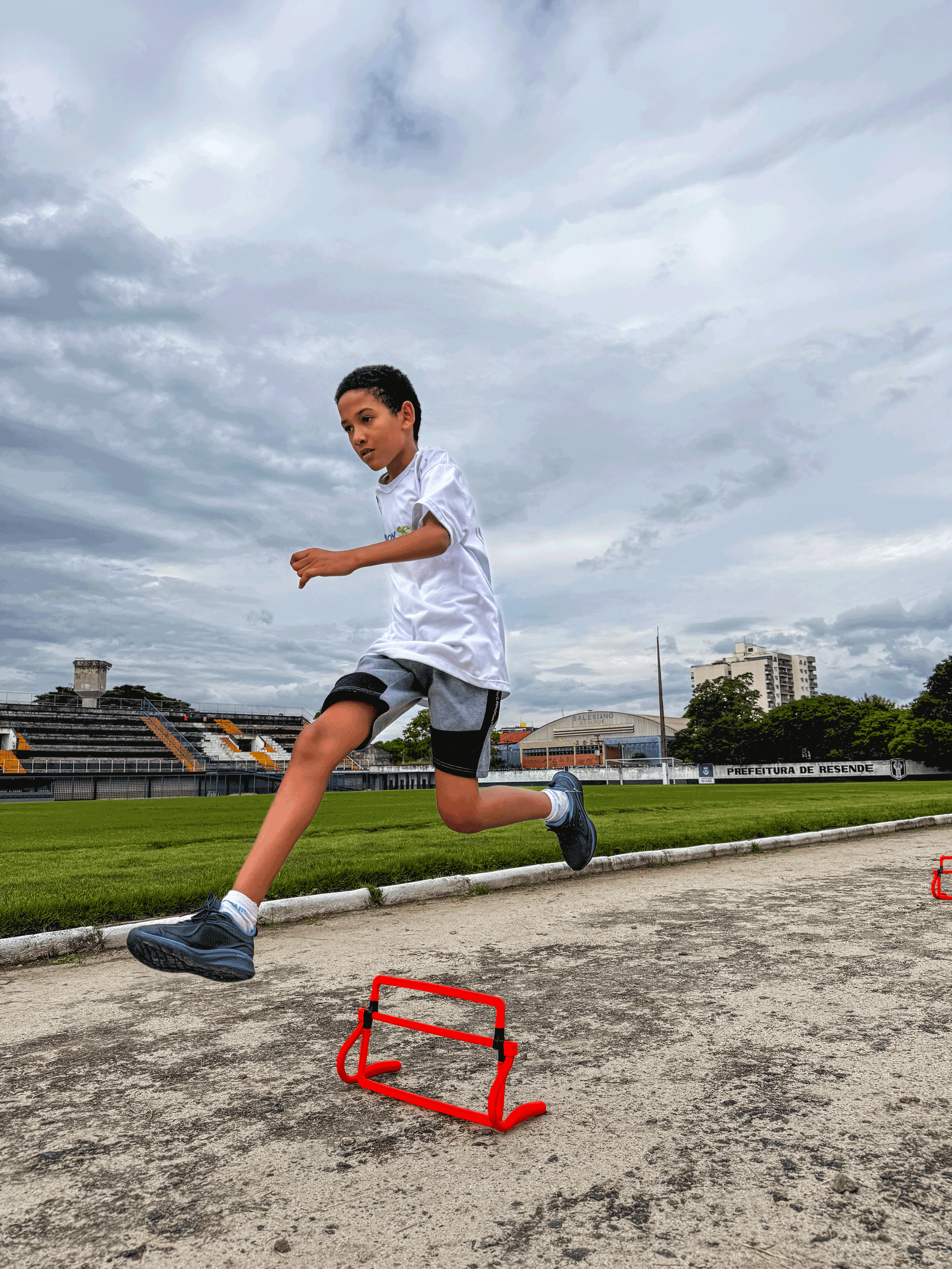 Menino pulando um obstáculo em uma pista, com céu nublado ao fundo.