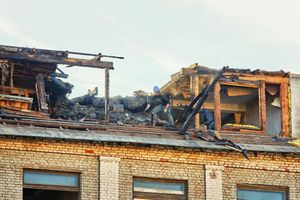 Two workers inspect the charred remains of a damaged brick building roof after a fire.